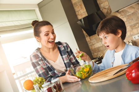 Family at home standing in kitchen together looking at spoon with salad laughing surprisedの写真素材