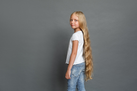 Little girl with long hair standing isolated on grey posing camera looking back confidentの写真素材