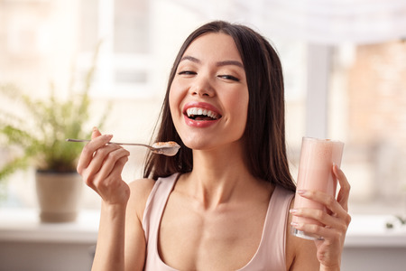 Young girl at kitchen healthy lifestyle standing with glass of shake looking camera laughing joyfulの写真素材
