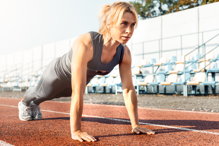 Sporty Lifestyle. Young woman on stadium doing plank smiling excitedの写真素材