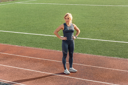 Sporty Lifestyle. Young woman wearing digital watch on stadium standing on track hands on hips smiling joyfulの写真素材