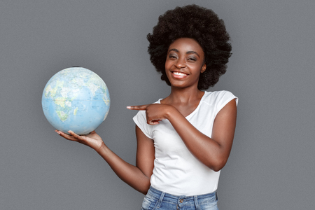 Young woman standing isolated on gray pointing at globe lets travel smiling happyの写真素材