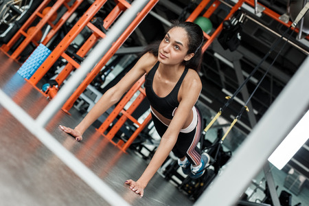 Young woman in gym sporty lifestyle standing on arms feet in suspansion straps doing push ups motivatedの写真素材