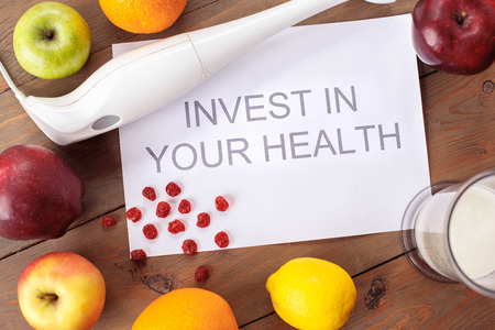 Invest in your health phrase on paper surrounded with fruits and hand blender healthy lifestyle top view close-upの写真素材
