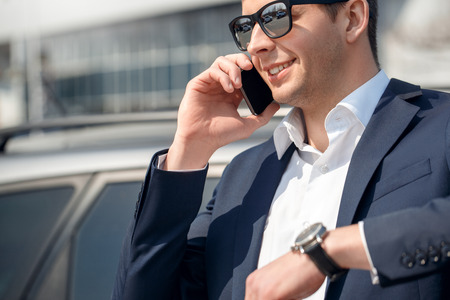 Young man in sunglasses leaning on car answering phone call cheerful close-upの写真素材