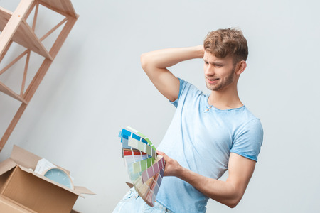 Young man moving to new place standing looking at palette smiling concernedの写真素材