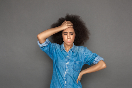Freestyle. Mulatto woman standing isolated on grey closed eyes touching head feeling painの写真素材
