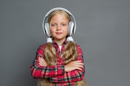 Little girl in headphones with ponytails standing isolated on grey crossed arms looking camera confidentの写真素材