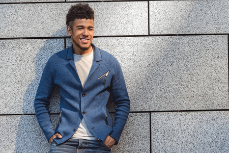 Freestyle. Mulatto guy standing isolated on wall hands in pockets smiling playfulの写真素材