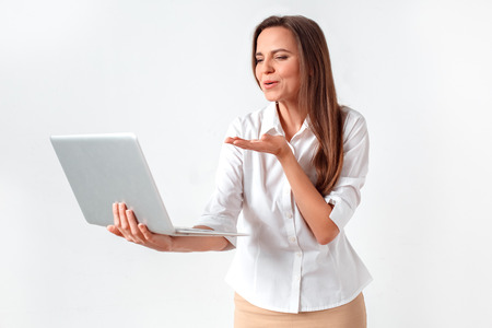 Romantic online communication. Woman standing isolated on white having video chat on laptop sending air kiss to camera happyの写真素材