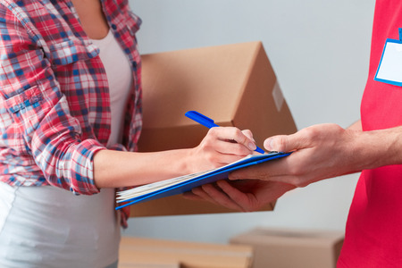 Young girl moving to new place standing with delivery man signing form close-upの写真素材