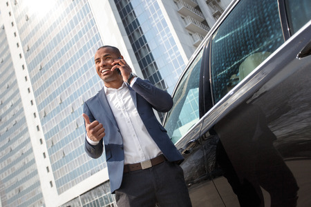 Young businessman standing near car answering phone call showing thumb up cheerful bottom viewの写真素材