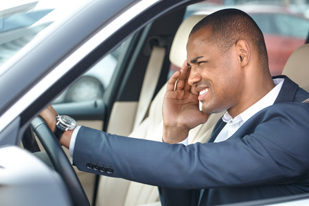 Young businessman driver sitting inside car driving touching head feeling pain side view in window close-upの写真素材