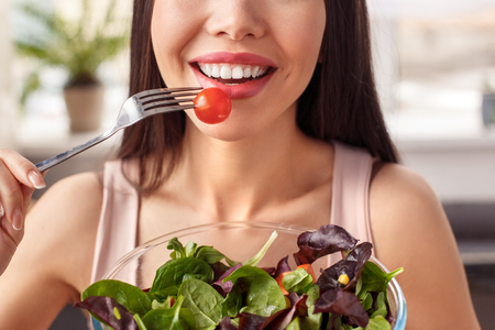 Young girl at kitchen healthy lifestyle standing with bowl eating salad happy face close-upの写真素材