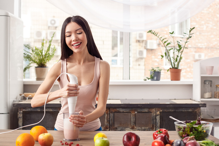 Young girl at kitchen healthy lifestyle standing blending milk smoothie with hand blender cheerfulの写真素材