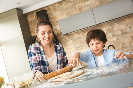 Family at home standing at table in kitchen together son playing with flour while mother rolling dough joyfulの写真素材