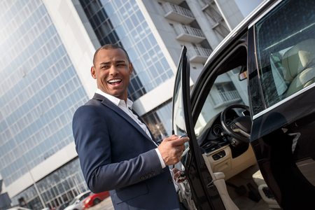 Young man standing opening car door with alarm key looking aside playfulの写真素材