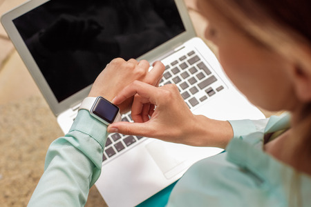 Young woman sitting on concrete stairs working on laptop checking time on digital watch close-up top viewの写真素材