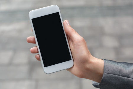 Young businesswoman standing on the city street showing screen of smartphone close-upの写真素材