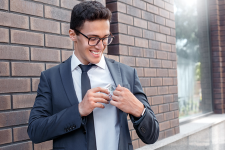 Business lifestyle. Businessman in eyeglasses standing on the city street putting salary into pocket cheerfulの写真素材