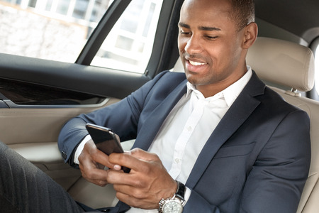 Young businessman sitting on back seat in car checking social media on smartphone cheerful close-upの写真素材