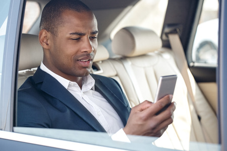 Young businessman sitting in car window opened checking social media on smartphone smiling joyfulの写真素材
