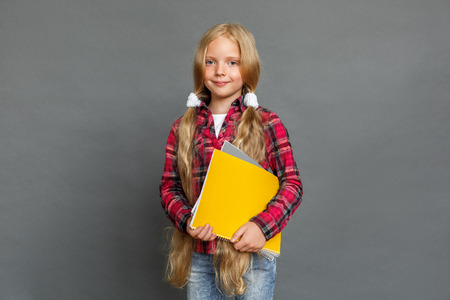 Little girl with ponytails standing isolated on grey with notebooks looking camera happy