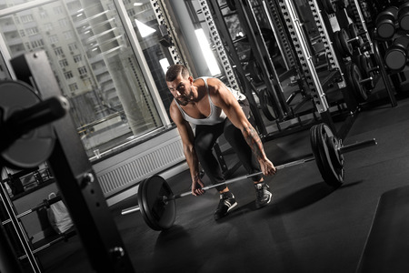 Bodybuilding. Bearded man exercising at gym bending down with barbell concentrated side view