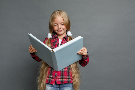 Little girl with ponytails standing isolated on grey reading book concentratedの写真素材