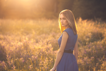 Recreation in Nature. Young woman in dress walking in the field looking back seriousの写真素材