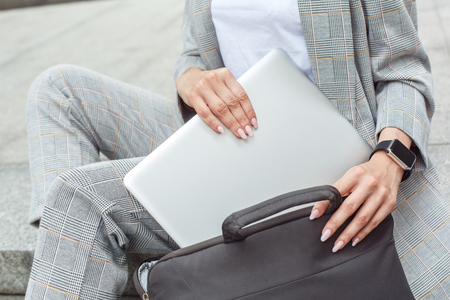 Young woman sitting on the city street putting laptop into case close-upの写真素材