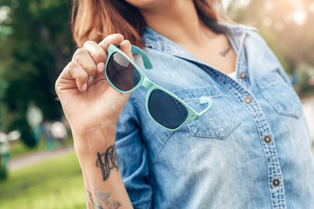 Young woman walking outdoors in the city park holding sunglasses close-upの写真素材