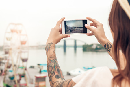 Young woman standing outdoors near seafront taking sight photo on smartphone close-up back viewの写真素材