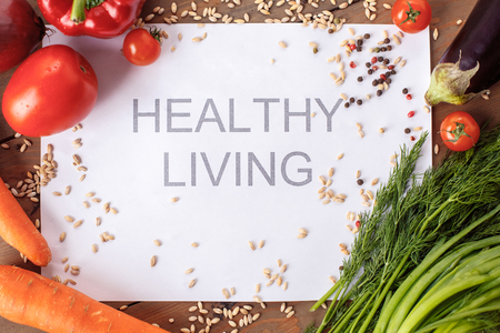 Healthy living phrase on paper surrounded with grains and vegetables on table top view close-upの写真素材