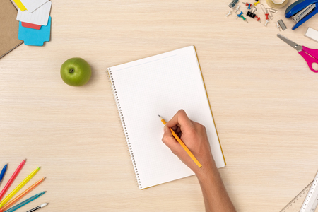 Wooden desk workplace top view person doing homework in notebook close-upの写真素材