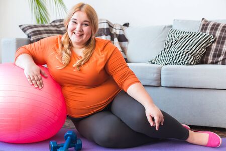 Chubby woman sport at home sitting leaning on ball smiling relaxedの写真素材