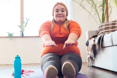 Chubby woman sport at home sitting on mat preparing for stretchingの写真素材