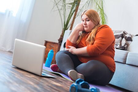 Chubby woman sport at home sitting looking at laptop boredの写真素材