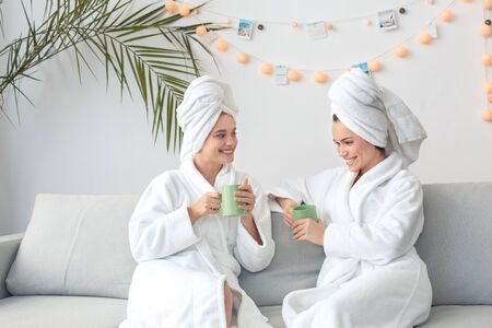 Friends together at home beauty care sitting in towels drinking coffee talking cheerfulの写真素材
