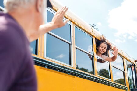 Father waving to daughter going to school by bus smiling cheerful