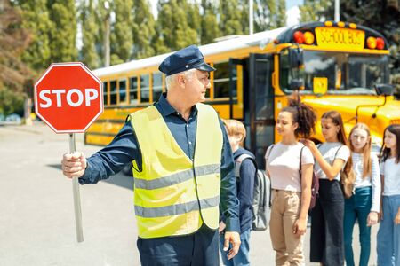 Group of children going out the school bus ready to cross the road while driver holding stop sign seriousの写真素材