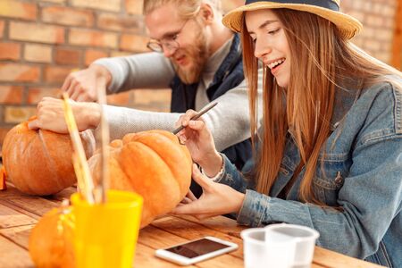 Young adult woman and man decorating ripe pumpkin for halloweenの写真素材