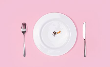 White plate with cigarette butt fork and knife isolated on pink backgrounf top view unhealthy habbitの写真素材