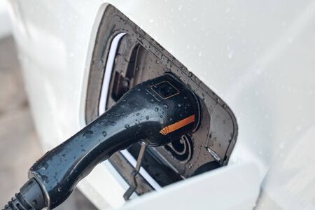 Close up view of black power cable supply plugged in white and new electric car. Charging...