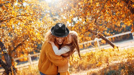 Cheerful and smiling ginger young adult mother holding hands with little daughter, looking at carved pumpkin with smoke and laughing. Woman making decoration for halloween with her charming childの写真素材