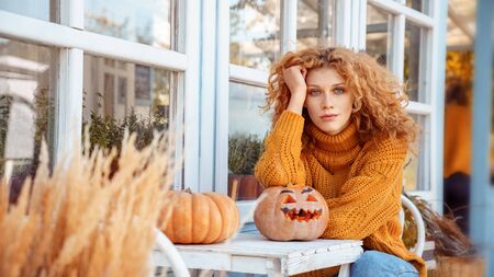 Young adult woman sitting behind table with carved pumpkinの写真素材