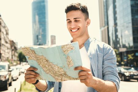 Outdoors Leisure. Stylish guy traveler standing on the street choosing route on map excited close-upの写真素材