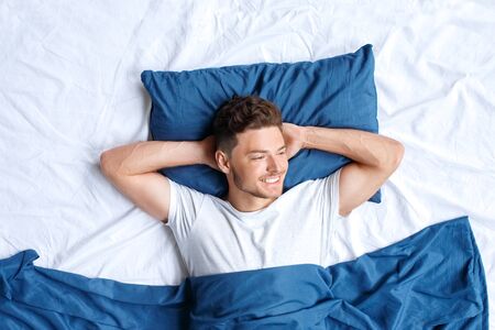 Bedtime. Guy lying on bed top view hands under head looking aside dreamfulの写真素材