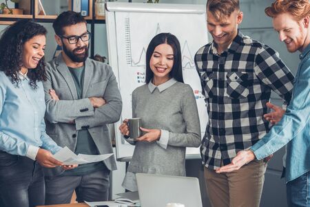 Startupers working together at office standing looking at laptop screen smiling joyfulの写真素材