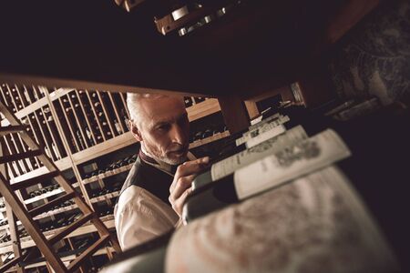 Sommelier Concept. Senior man standing choosing wine concentrated close-up
